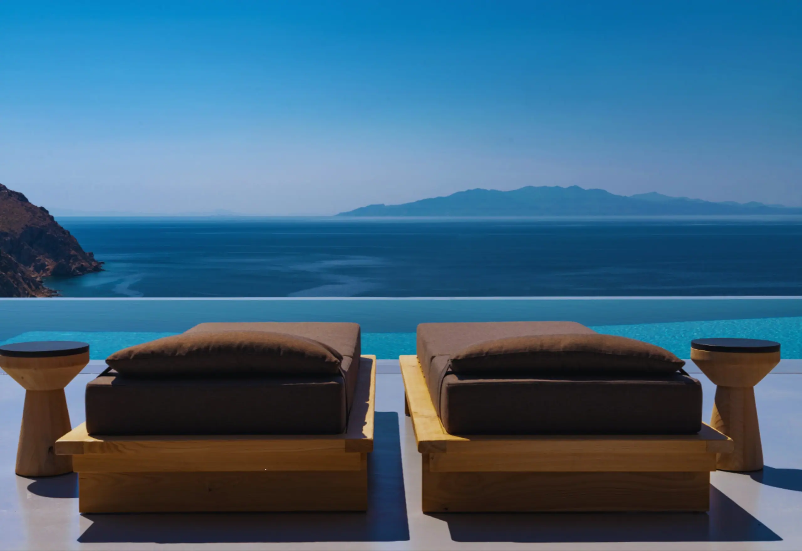 Two daybeds at the edge of a pool facing the Aegean