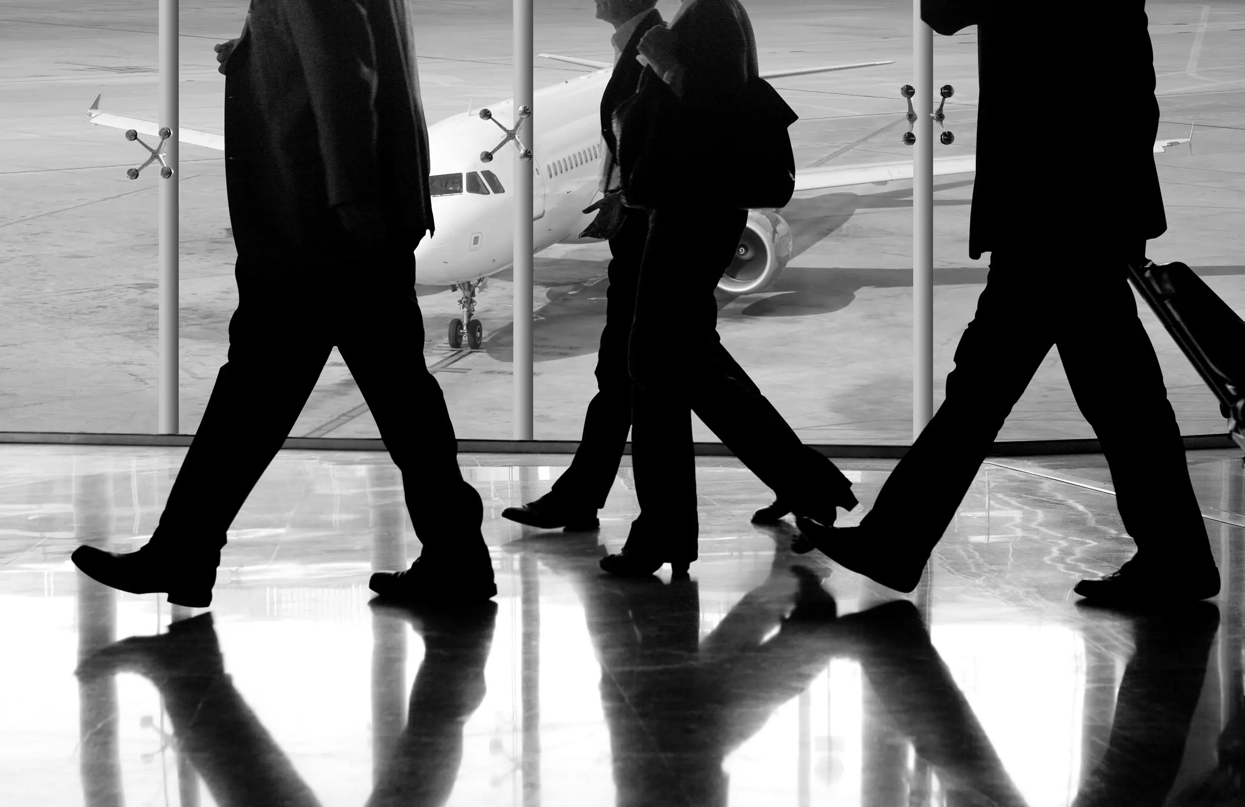 Travellers walking through an airport terminal, an airliner beyond the glass