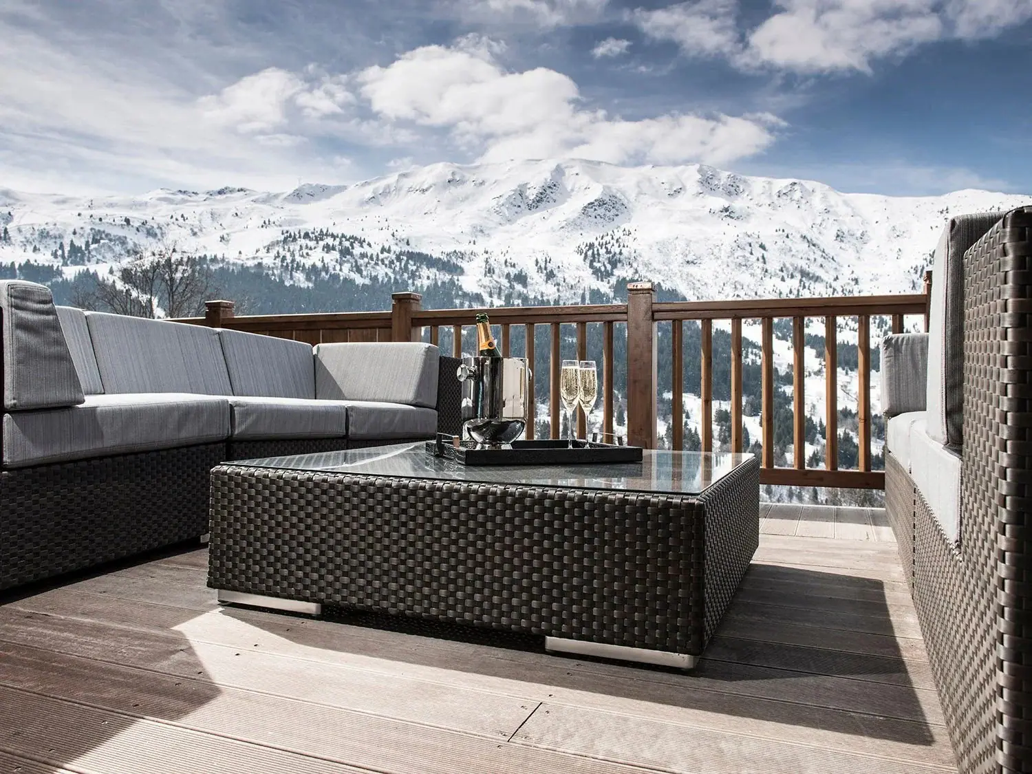 A balcony lounge with champagne on ice, facing a snow-covered mountain ridge under a bright sky