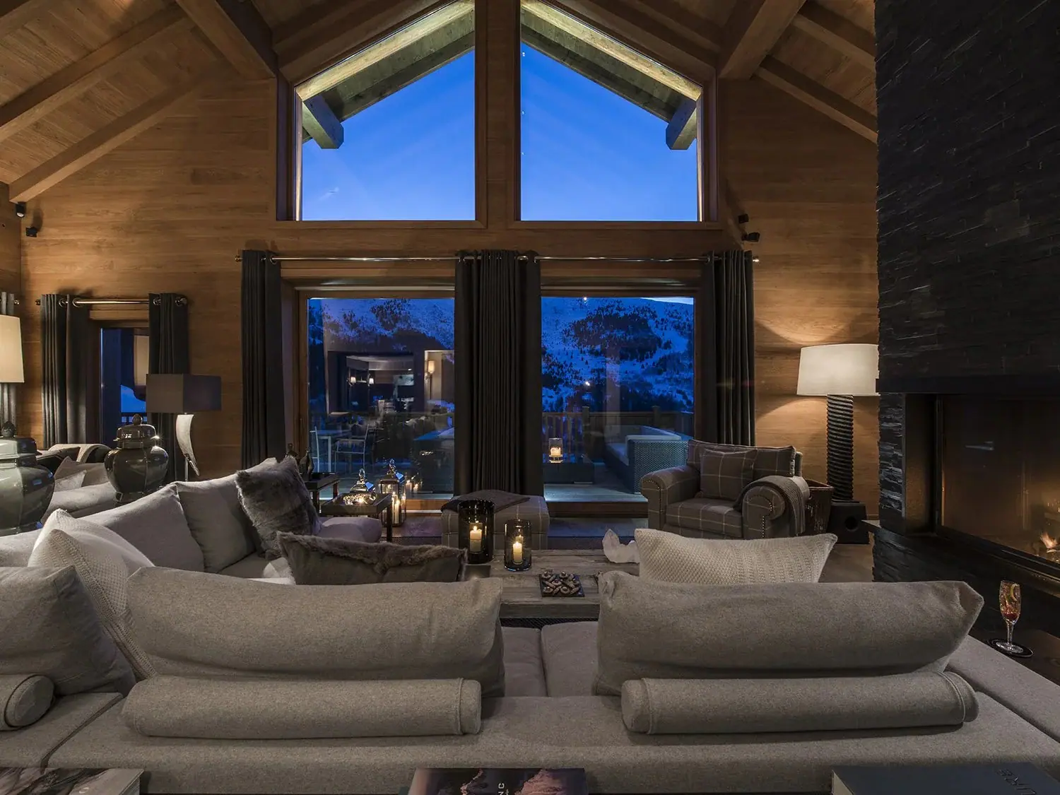 A chalet living room with tall tiered windows facing the mountains