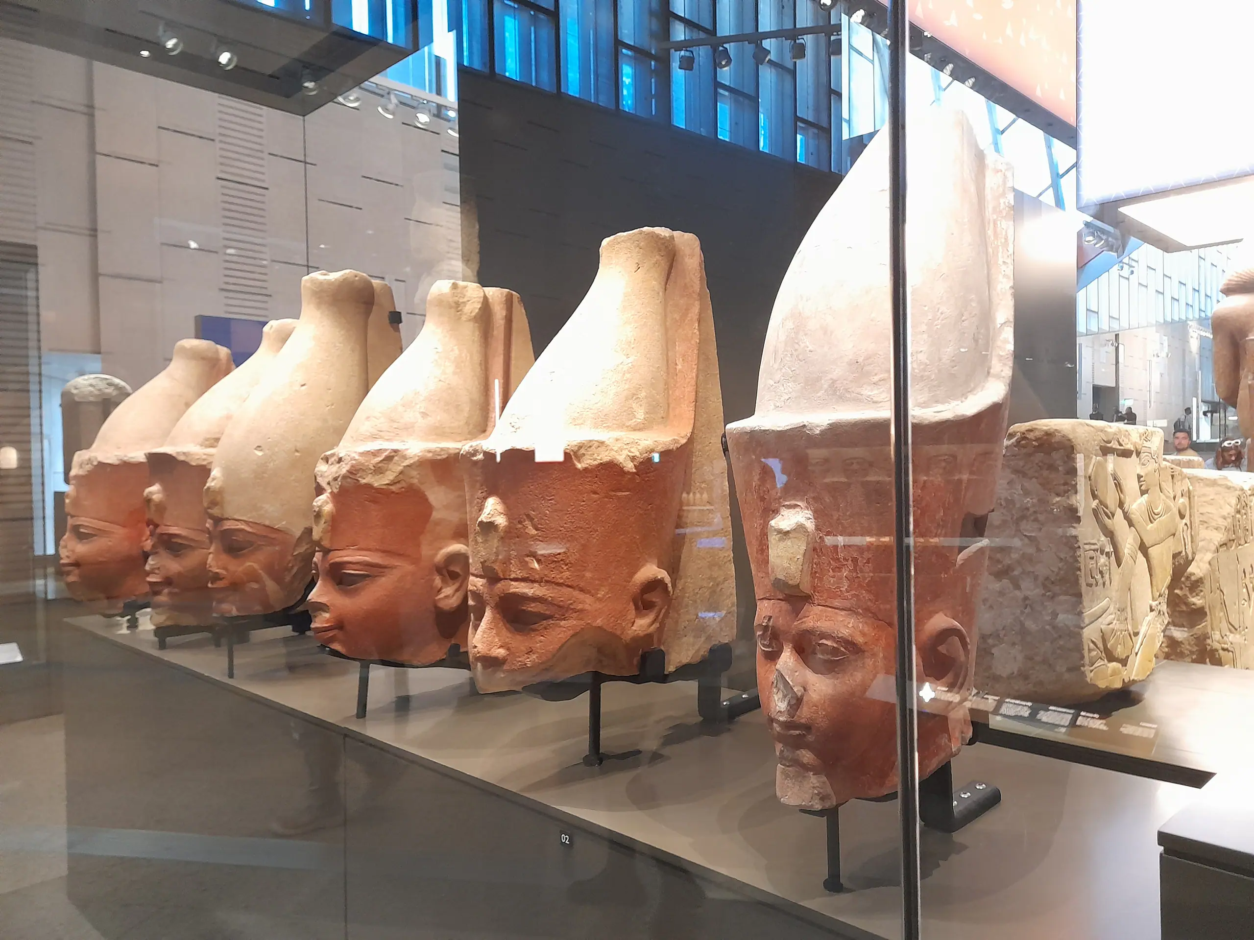 A row of colossal red granite royal heads on display at the Grand Egyptian Museum