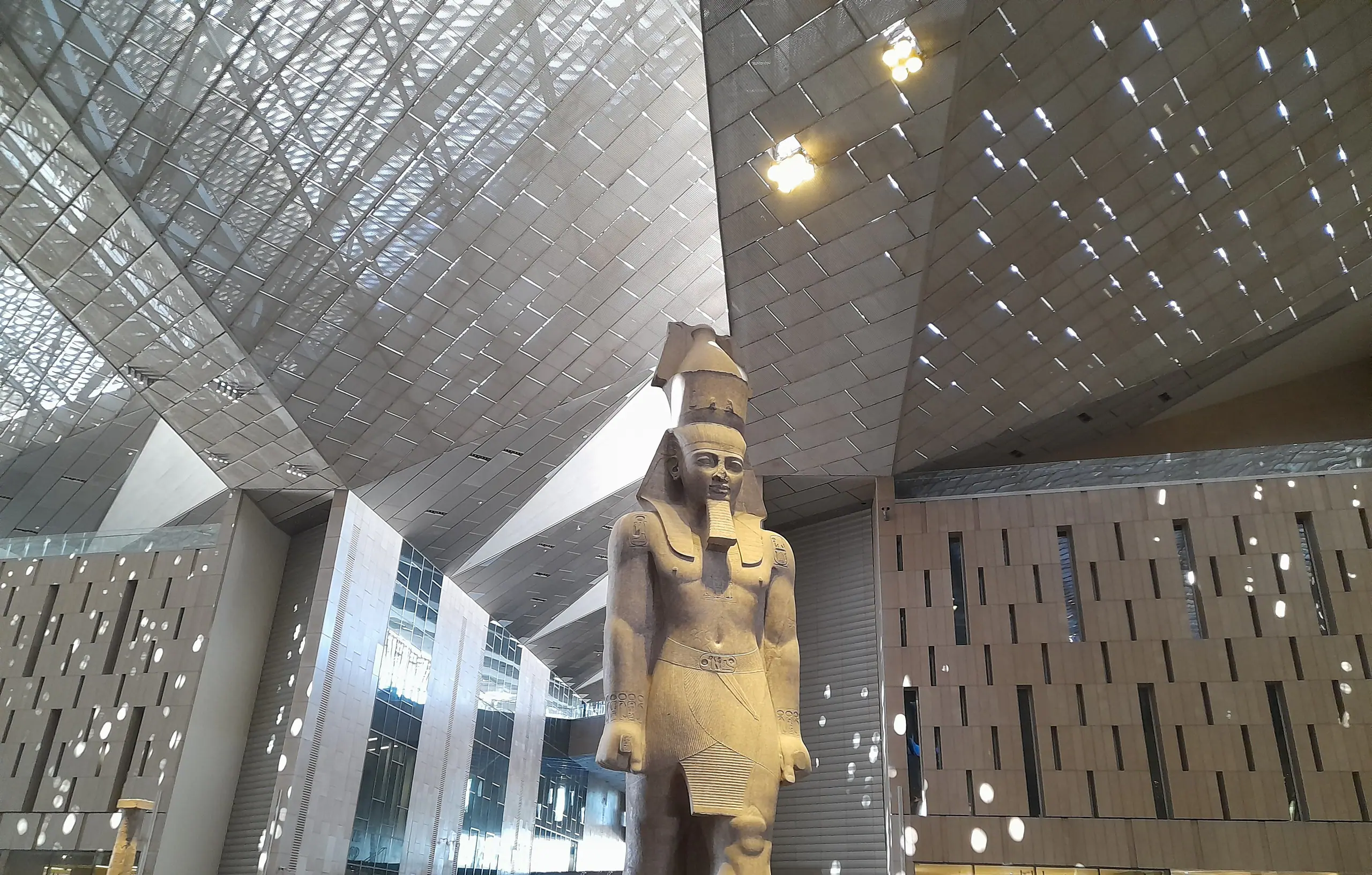 The colossal statue of Ramesses II beneath the faceted roof of the Grand Egyptian Museum’s Grand Hall