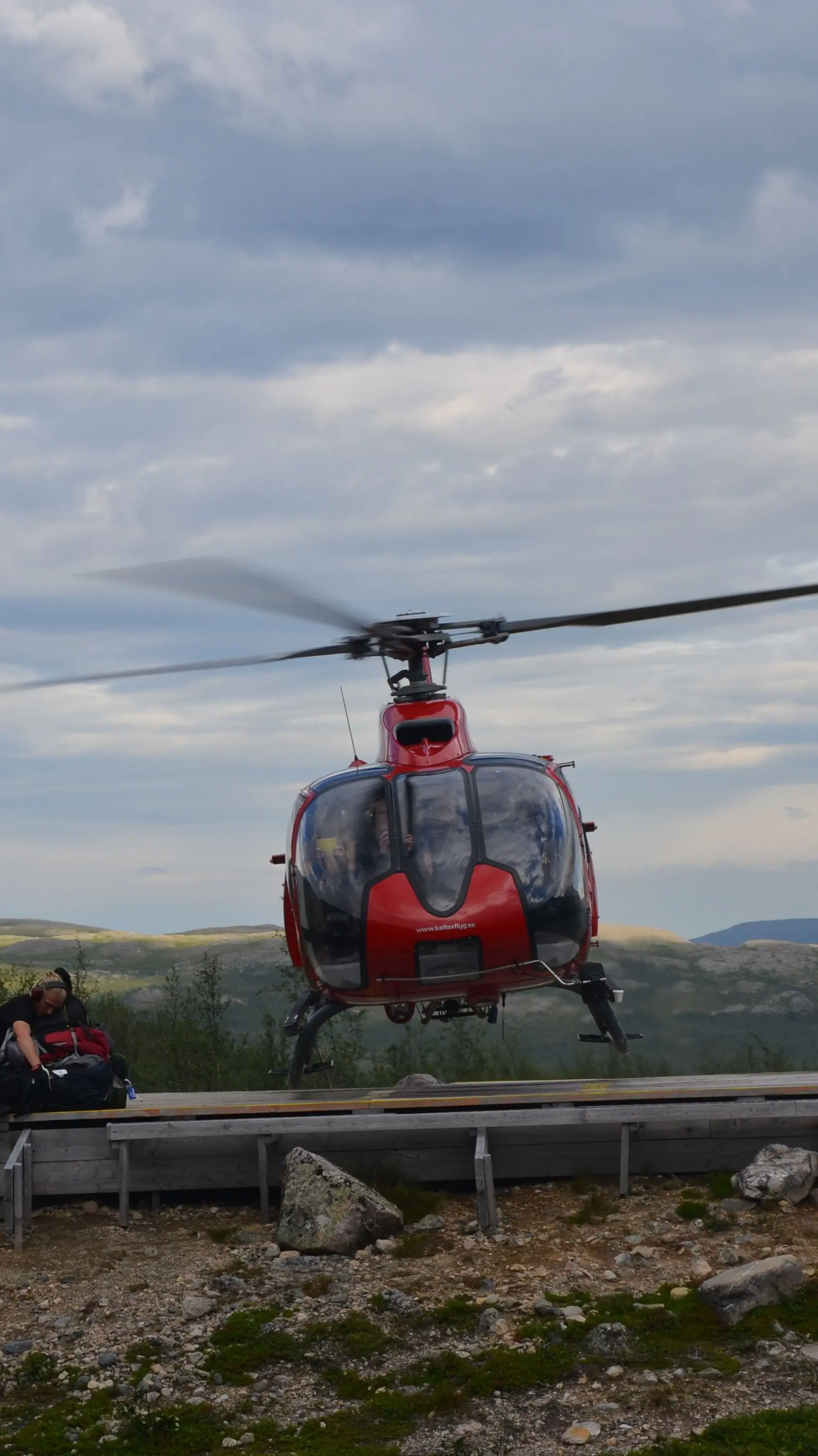 A helicopter landing on a mountain helipad in Swedish Lapland, bags waiting beside it