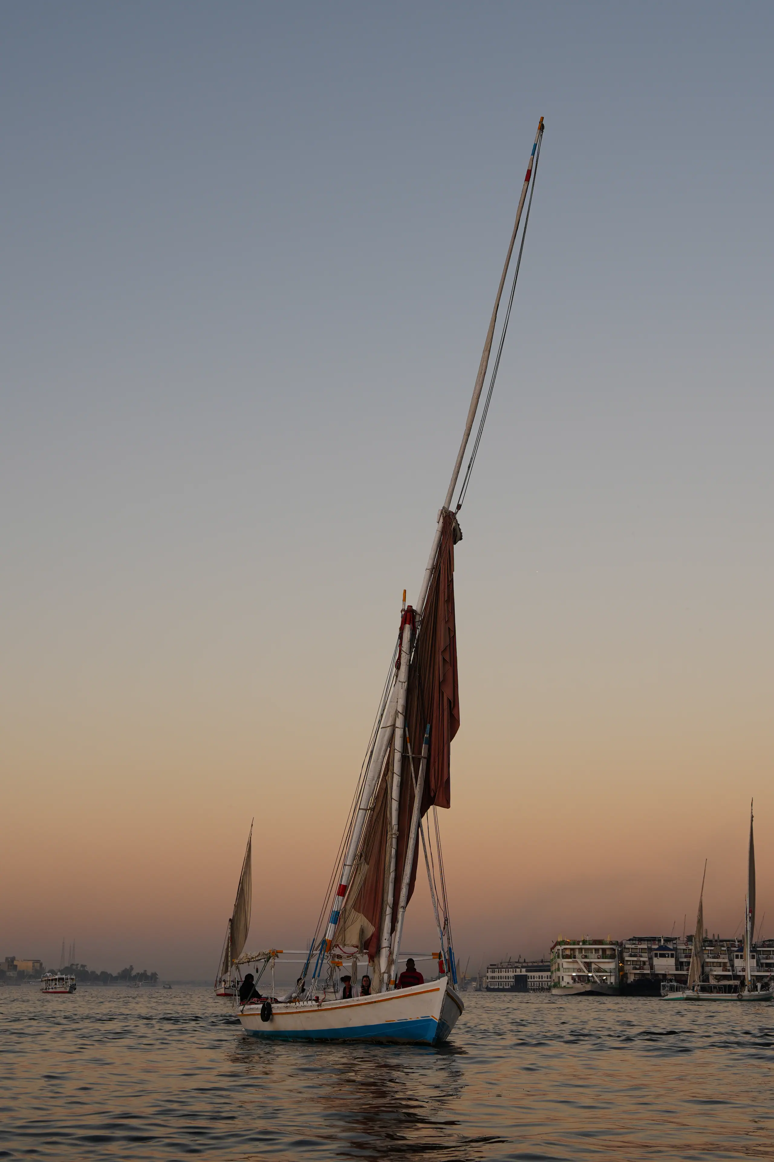 A felucca on the Nile at Luxor at dusk, Nile boats moored beyond