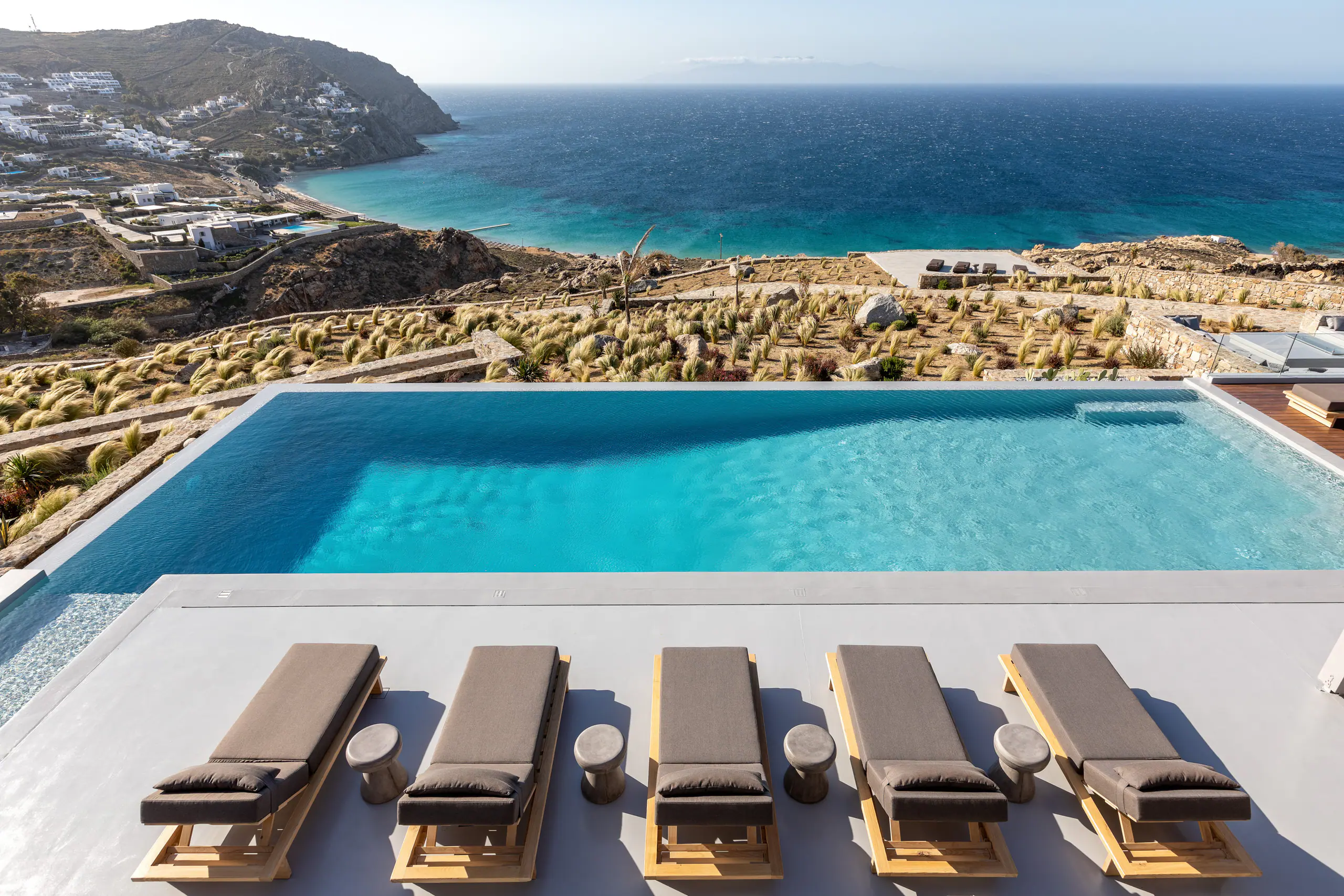 The infinity pool at Villa Serenade with a row of sun loungers, looking over a bay and the Aegean Sea, Elia, Mykonos